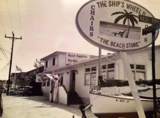 Historic photo of Harvey Cedars: The Ship's Wheel beach store with its oval sign, a sailboat, and Long Beach Boulevard